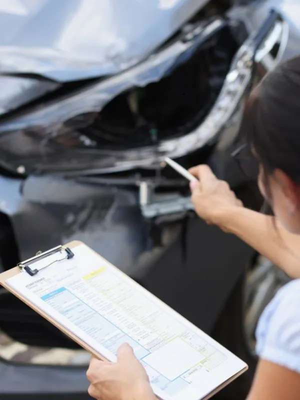 Car inspection: an inspector with a clipboard checking the damaged front of a used car