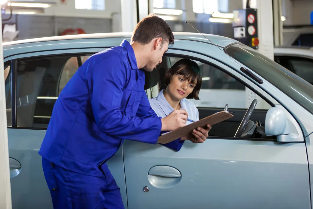 Mechanic showing a clipboard to a woman sitting in her car