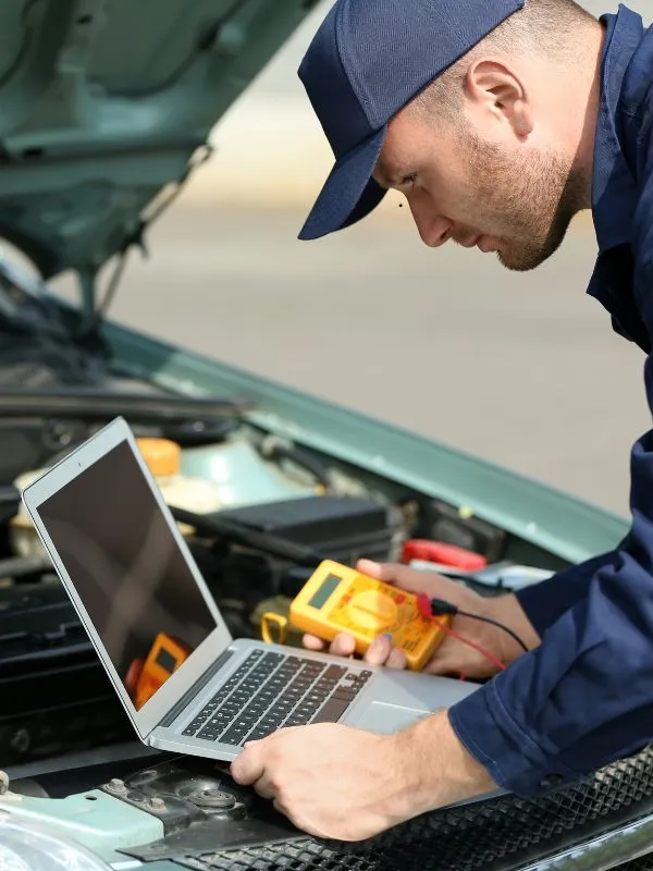 Mechanic running engine diagnostics on a laptop under the bonnet