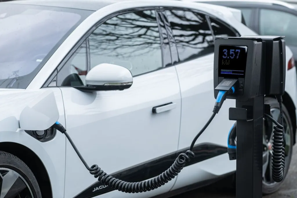 White electric SUV plugged into a charging post whose screen shows the charge