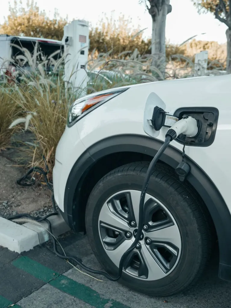 White electric SUV at an outdoor charging bay, the cable plugged in above its front wheel