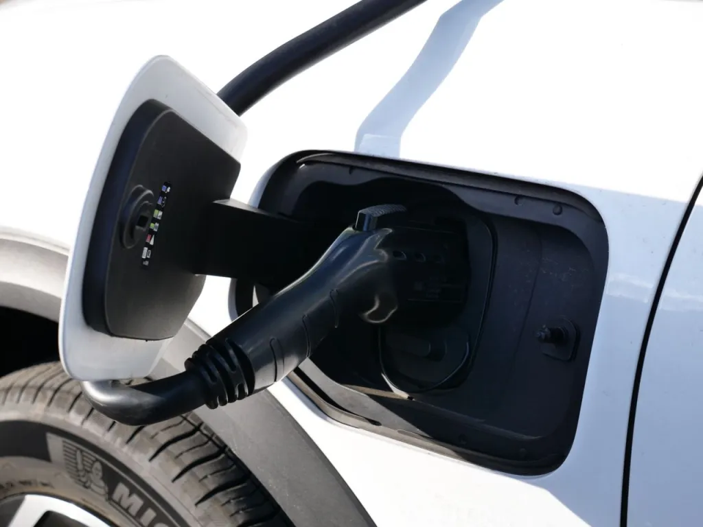 Close-up of a charging connector plugged into the open charge port of a white electric car