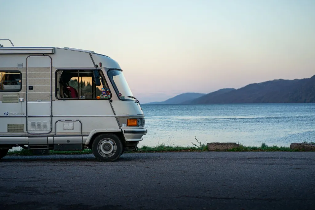 White motorhome parked by the water at dusk, with hills on the far shore