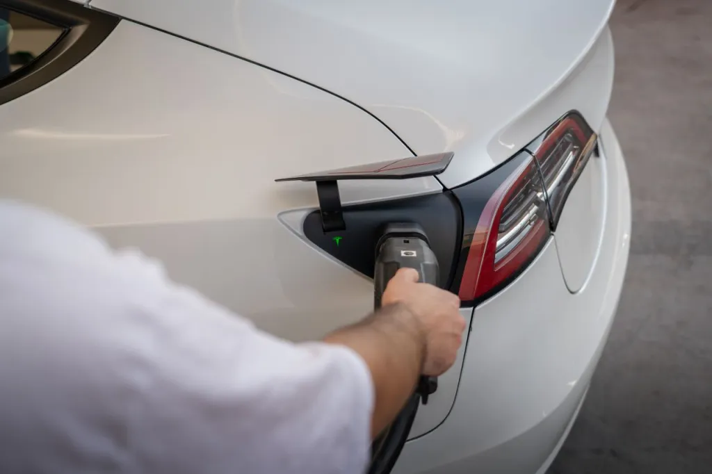 Hand plugging a charging connector into the charge port of a white electric car