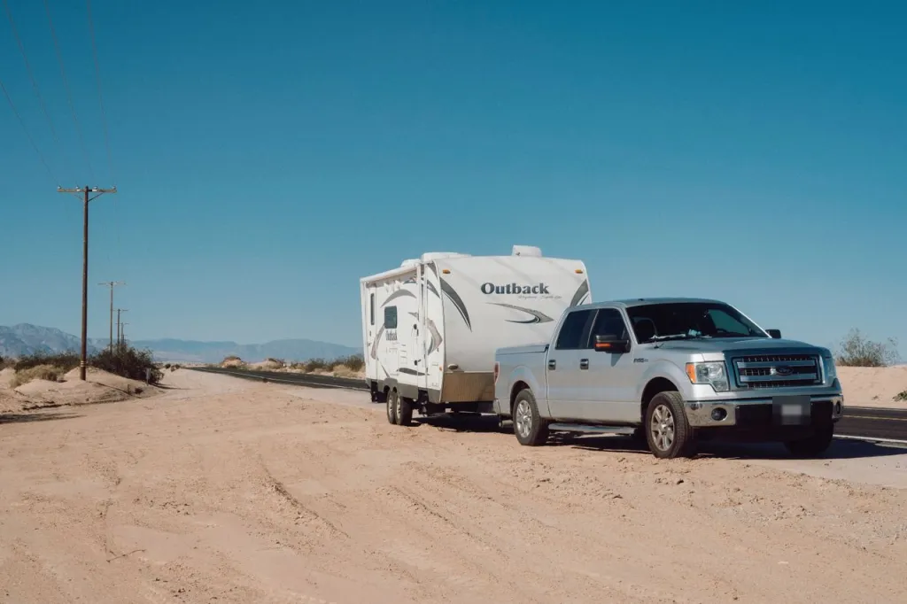 Silver pickup towing a white caravan, stopped beside a desert road