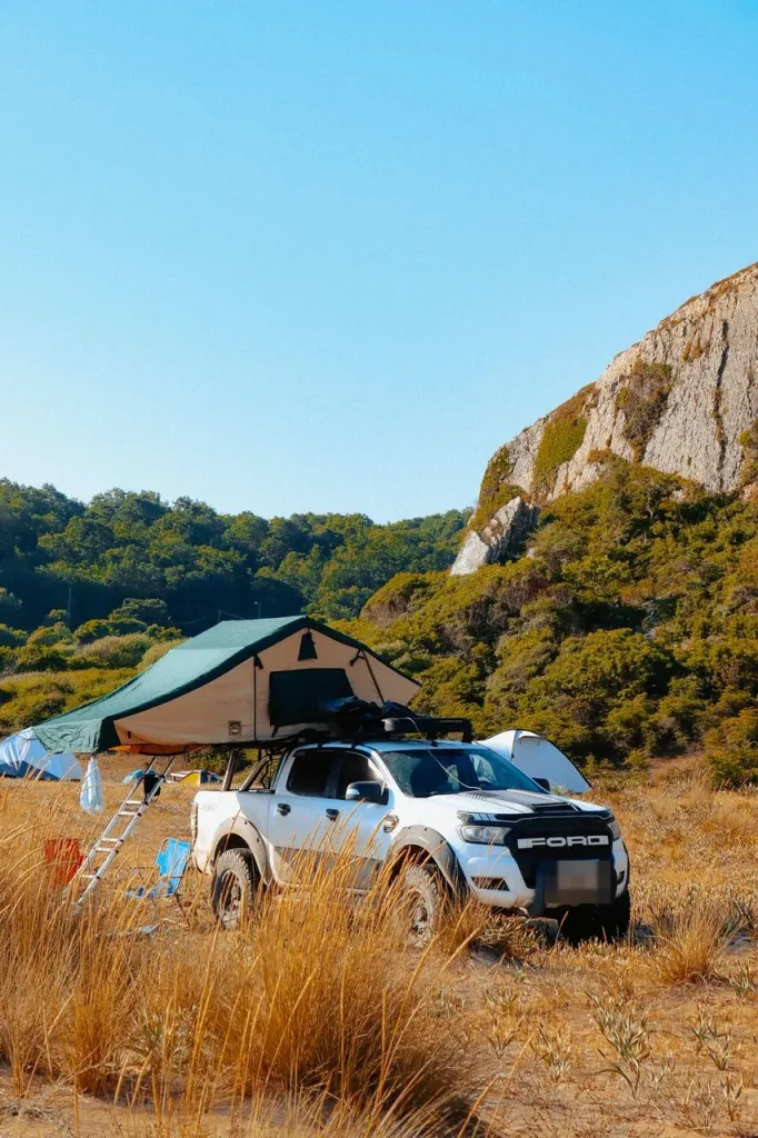 White Ford Ranger ute with a rooftop tent set up at a campsite in long dry grass
